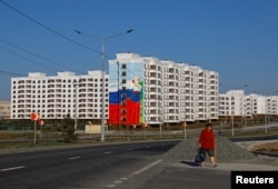 Жінка крокує повз новозведені будинки в Маріуполі. Місцеві жителі розповідають, що нове житло переважно віддають під іпотеку для жителів РФ