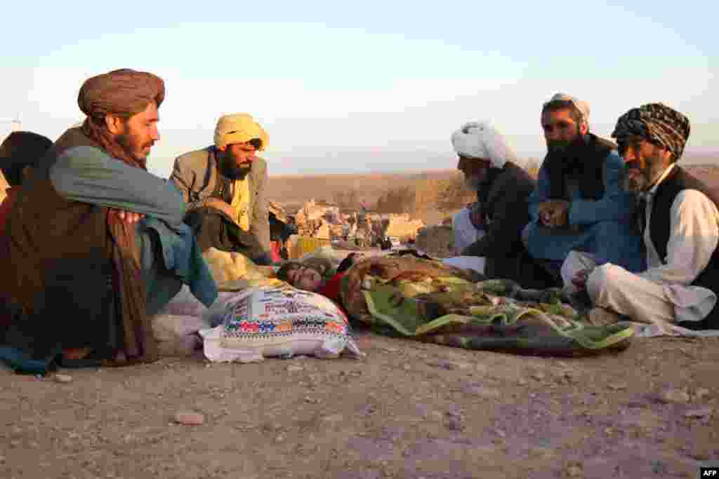 شماری از مردان در قریه سربلند ولسوالی زنده جان هرات در اطراف اجساد اقارب شان که در زلزله روز شنبه جان باخته نشسته اند
