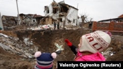 Діти дивляться на воронку, яка залишилася внаслідок російського ракетного удару у Глевасі на Київщині, 26 січня 2023 року
