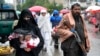 یک زن در یکی از بازار‌های افغانستان در حال قدم زدن و یک نیروی طالبان با تفنگ